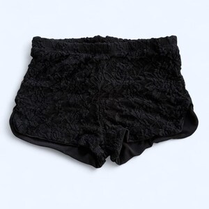 May include: Black lace shorts with an elastic waistband. The shorts have a floral pattern and a solid black lining. The garment is designed for comfort and style.