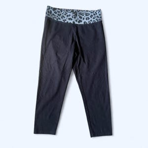 May include: Black leggings with a leopard print waistband. The leggings are cropped at the calf and have a solid black color. The waistband features a gray and black leopard print pattern.