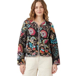 May include: A black quilted jacket with a colourful floral design in pink, blue, yellow, and green. The jacket features a V-neck, long sleeves, and white trim. The model is wearing white trousers.
