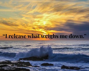 May include: A scenic image of a sunset over the ocean. The sky is a mix of blue, orange, and yellow hues, with the text "I release what weighs me down." The waves crash against the dark rocks in the foreground.