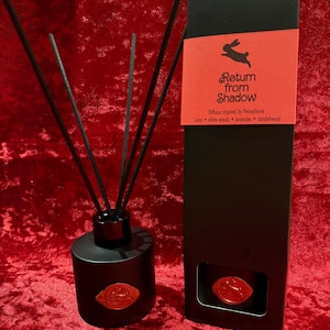 Könnte beinhalten: Schwarze Diffusorflasche mit Stäbchen und passender Schachtel. Die Schachtel hat ein rotes Etikett mit dem Text "Return from Shadow" und einem Kaninchenlogo. Der Diffusor ist von Persephone inspiriert und enthält Lotus, Weißholz, Lavendel und Sandelholz.
