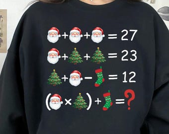 Op de afbeelding: Zwart sweatshirt met een kerstthema. De afbeelding toont een reeks wiskundige vergelijkingen met Sinterklaasgezichten, kerstbomen en kousen. De laatste vergelijking eindigt met een vraagteken.
