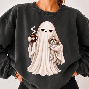 Op de afbeelding: Een antracietgrijze sweater met ronde hals en een afbeelding van een witte geest met een verveelde uitdrukking die een bruine koffiemok met de tekst MEH vasthoudt en een kleine bruin-witte Shih Tzu in zijn gedrapeerde armen draagt.