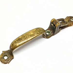 May include: A brass door handle with a curved handle and a latch mechanism. The handle is tarnished and has a worn finish.