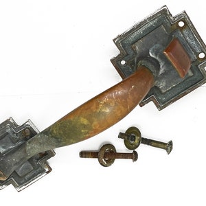 May include: Antique brass door handle with a square, ornate backplate and three screws. The handle is a curved,  elongated shape.