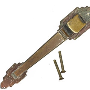 May include: A vintage brass door handle with an ornate design. The handle is attached to two screws.