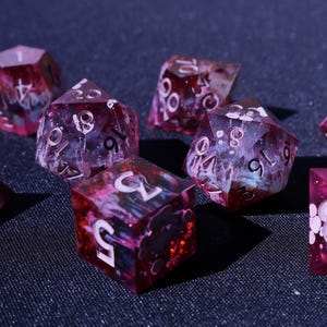 May include: A collection of polyhedral dice in various shapes, including D4, D6, D8, D10, D12, and D20. The dice are a translucent red with white numbering and a swirling, galaxy-like interior. Ideal for tabletop gaming.