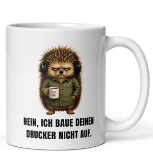 Könnte beinhalten: Ein weißer Keramikbecher mit einer Grafik eines mürrischen Igels, der schwarze Kopfhörer und ein grünes Hemd trägt und eine kleine Kaffeetasse hält. Unter dem Igel steht der Text: NEIN, ICH BAUE DEINEN DRUCKER NICHT AUF. Der Becher hat einen Henkel.