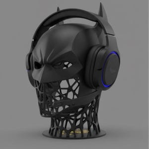 May include: A black Batman-themed headphone stand. The stand is shaped like Batman's head, with the ears of the bat extending upwards. The headphones are black with blue accents. The base of the stand has a unique, open design.