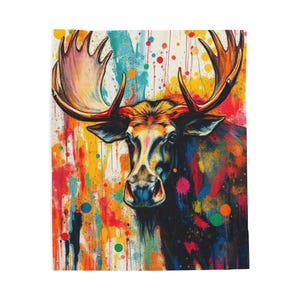 Puede incluir: Una colorida manta con una pintura vibrante de un alce. La obra de arte muestra un alce con grandes astas, representado en una mezcla de colores brillantes, incluyendo rojo, amarillo, azul y verde. El fondo es una salpicadura de pintura.
