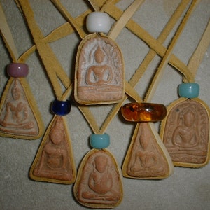 K&ouml;nnte beinhalten: Sieben kleine, braune Tonanh&auml;nger mit Buddha-Bildern, jeweils an einer Lederschnur mit einer Glasperle. Die Perlen sind blau, lila, t&uuml;rkis und bernstein.
