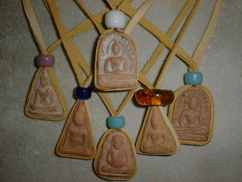 K&ouml;nnte beinhalten: Sieben kleine, braune Tonanh&auml;nger mit Buddha-Bildern, jeweils an einer Lederschnur mit einer Glasperle. Die Perlen sind blau, lila, t&uuml;rkis und bernstein.
