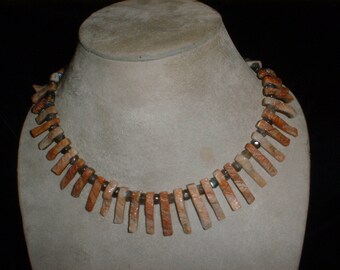 May include: A necklace made of light brown and orange stone beads with dark grey accents.
