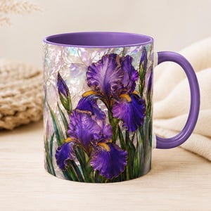 Può includere: Una tazza in ceramica con una vivace illustrazione di fiori di iris viola intenso con accenti gialli e steli verdi. La tazza presenta un manico e un interno viola a tinta unita, su uno sfondo che ricorda la madreperla iridescente.