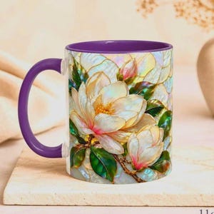 May include: A ceramic mug with a purple handle and interior, featuring a vibrant, iridescent-style illustration of white magnolia flowers with pink centers and green leaves against a shimmering, pearlescent background. The mug has an 11oz capacity.