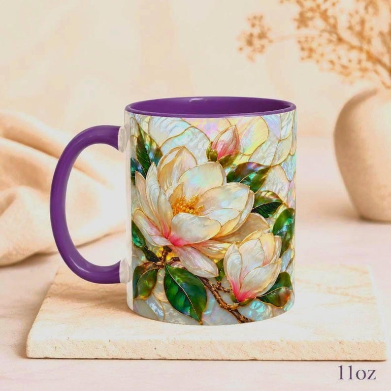 May include: A ceramic mug with a purple handle and interior, featuring a vibrant, iridescent-style illustration of white magnolia flowers with pink centers and green leaves against a shimmering, pearlescent background. The mug has an 11oz capacity.