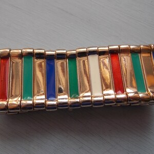May include: A gold-toned bracelet with alternating colored enamel bars. The bars are red, white, blue, and green.