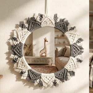 May include: Round macrame mirror with a woven design in white and gray. The mirror is hanging on a white wall. The mirror reflects a room with a wooden giraffe statue on a table.