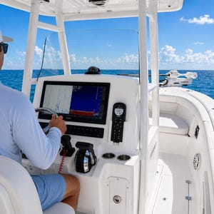 May include: A white motorboat with a blue sky and ocean background. The boat's dashboard features a large screen displaying data, a steering wheel, and various controls. The boat is designed for recreational use on the water.