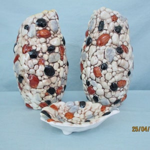May include: Two white ceramic vases with a pebble design in shades of brown, black, and orange. A matching white ceramic dish with a pebble design is in the foreground.