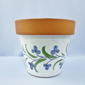 May include: A white ceramic flower pot with a brown rim and a blue and green floral design.