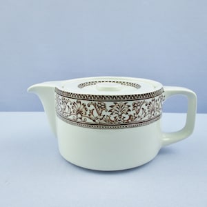 May include: White ceramic teapot with a brown floral pattern around the middle. The teapot has a lid and a handle.