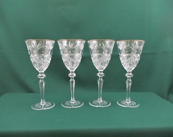 May include: Set of four clear glass wine glasses with a gold rim. The glasses have a cut crystal design.