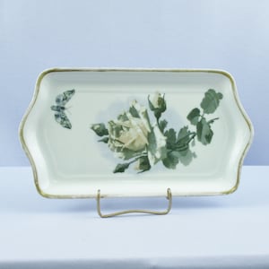 May include: A white porcelain serving tray with a gold rim. The tray features a painted design of a white rose with green leaves and a butterfly.