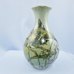 May include: A ceramic vase with a crackled glaze finish. The vase is decorated with a hand-painted design of birds in flight on branches. The vase is a light green color with gold accents.