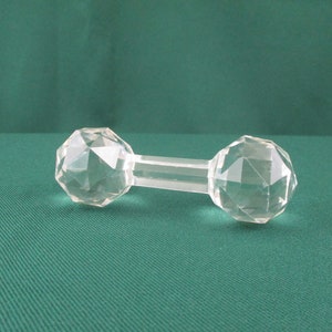 May include: A clear glass dumbbell with faceted sides. The dumbbell is on a green surface.