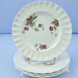 May include: Set of four white ceramic dinner plates with a raised, woven pattern and floral design in shades of pink, purple, and green.