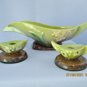May include: A set of three vintage ceramic candle holders in a green and brown glaze. The holders feature a stylised leaf design with floral accents.