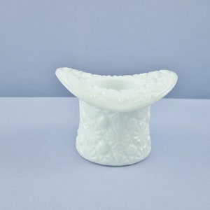 May include: A white milk glass top hat shaped vase with a floral design.