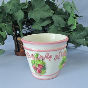 May include: White ceramic planter with pink trim and a raised design of pink and green berries and leaves.