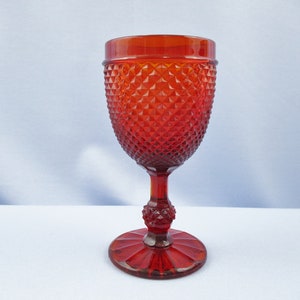 May include: A red glass goblet with a diamond pattern. The goblet has a tall stem and a wide base.