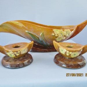 May include: A set of three vintage ceramic pieces in a brown and yellow glaze with a floral design. The set includes a large bowl and two candle holders.