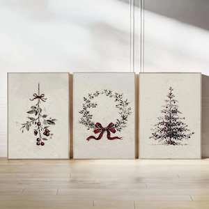 Puede incluir: Tres impresiones navideñas enmarcadas de estilo vintage. Las impresiones presentan una ramita de bayas, una corona con un lazo rojo y un árbol de Navidad. La obra de arte es en tonos de rojo, negro y crema.