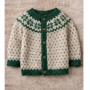 May include: A cream-coloured baby cardigan with a green yoke and trim. The sweater features a repeating pattern of green floral designs on the yoke and small green dots throughout the body. It has a button-up front with wooden buttons.
