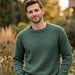 May include: A green crew neck sweater. The sweater has long sleeves and a textured knit. The person in the image is wearing the sweater. The background is blurred with natural light.