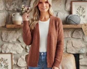 Può includere: Un cardigan aperto color ruggine con maniche lunghe e orlo a coste, indossato sopra un top bianco semplice e jeans blu. Il cardigan è realizzato in un morbido tessuto a maglia testurizzato con una scollatura senza colletto.