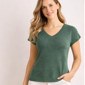 May include: A green short-sleeve sweater with a V-neck. The sweater has a textured knit pattern on the sleeves and a ribbed hem. The woman is wearing white pants.