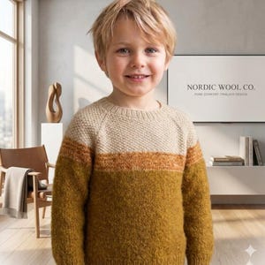 Könnte beinhalten: Ein Kind trägt einen beigen, orangefarbenen und senfgelben Pullover. Der Pullover hat ein strukturiertes Strickmuster und einen Rundhalsausschnitt. Im Hintergrund ist der Text "NORDIC WOOL CO. PURE COMFORT. TIMELESS DESIGN." zu sehen.