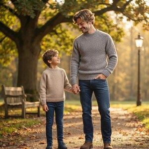 Könnte beinhalten: Eine große Person in einem grauen, langärmeligen Strickpullover und blauen Jeans steht neben einer kleineren Person in einem beigen, langärmeligen Strickpullover und blauen Jeans, wobei beide Händchen haltend auf einem Parkweg stehen.