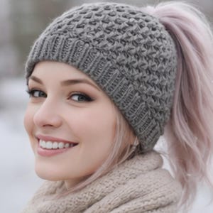 May include: A grey knit beanie with a textured, waffle-like pattern and a ribbed hem. The hat features an opening at the crown designed to accommodate a ponytail, allowing hair to pass through while keeping the head warm in cold weather.