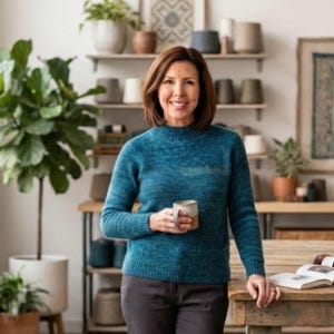 May include: A teal long-sleeved sweater with a ribbed mock neck, cuffs, and hem. The sweater features a textured knit pattern and is worn with dark gray trousers. A ceramic mug is held in one hand, and an open book rests on a wooden table.