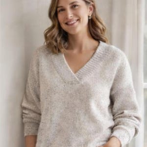 Può includere: Un maglione beige chiaro con scollo a V con un motivo a maglia strutturato. Il maglione ha maniche lunghe e uno scollo a coste. La modella indossa il maglione. Il maglione è realizzato in un materiale morbido e confortevole.