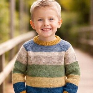 May include: A smiling child wears a striped sweater with bands of blue, green, tan, and yellow. The collar and cuffs are yellow. The background is a blurred outdoor scene. The sweater is suitable for children.