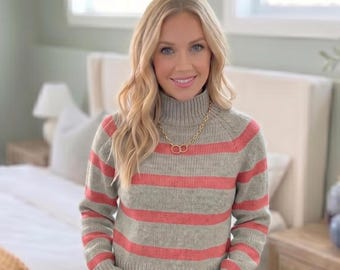 May include: A grey and coral striped sweater with a high turtleneck collar and long sleeves. The sweater features a ribbed knit texture and is paired with a gold-toned chain necklace featuring two interlocking circular pendants at the center.