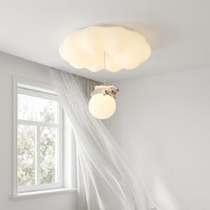 May include: A whimsical ceiling light fixture featuring a cloud-shaped shade and a hanging globe. A small stuffed bear rests on the globe. The light fixture is white and designed for a child's room. The room has a window with white curtains.