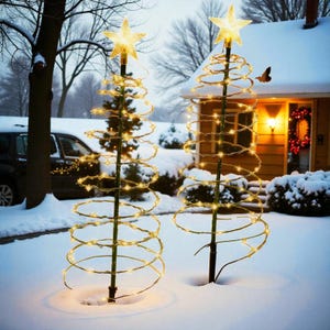 May include: Two outdoor Christmas tree decorations. Each tree is made of a spiral wire frame wrapped with warm white lights. A gold star tops each tree. The trees are set in the snow in front of a house.